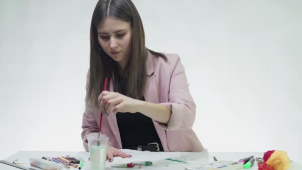 매력적 인 젊은 여자가 흰 스튜디오 에 있는 책상 위에 놓여 있는 백지에 아크릴 페인트 로 그림을 그린다 — 비디오