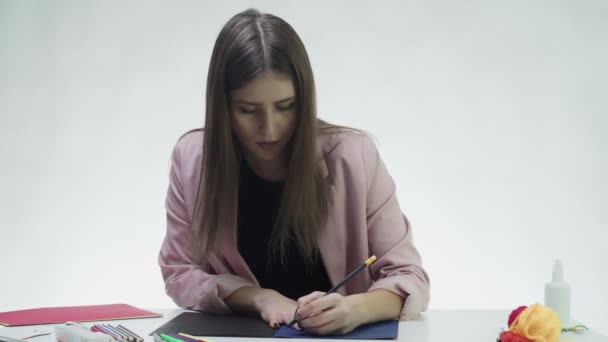 Atractiva mujer joven dibuja con pinturas acrílicas en un papel blanco en la mesa en un estudio blanco — Vídeo de stock