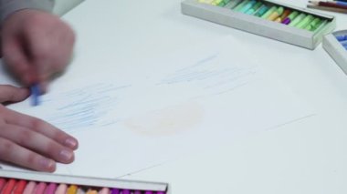 Ressamın en iyi görüntüsü beyaz bir stüdyoda beyaz bir kağıt üzerine pastel çizer.