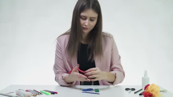 매력적 인 젊은 여성이 화이트 스튜디오에 있는 테이블에서 플라스틱을 가지고 무엇인가를 만든다 — 비디오