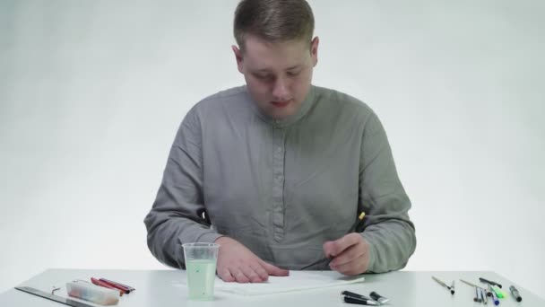 Jeune homme dessine avec une peinture acrylique rouge sur un chiffon blanc à la table dans un studio blanc — Video