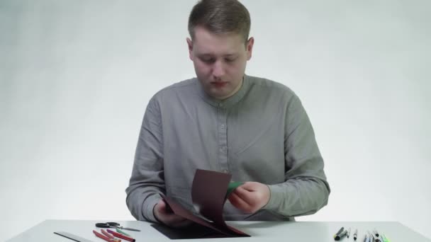Młody człowiek używa ołówka i linijki do rysowania linii na zielonym papierze przy stole w białym studiu — Wideo stockowe
