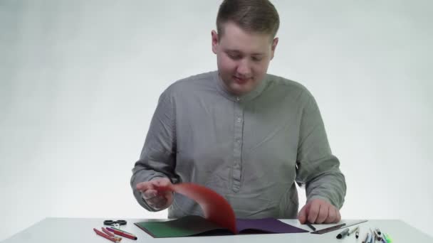 Joven utiliza lápiz para dibujar en un papel de color naranja en la mesa en un estudio blanco — Vídeo de stock