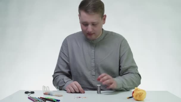 Jeune homme déroule une ligne métallique et la prépare à perler à la table dans un studio blanc — Video