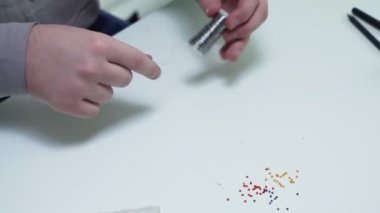 Bir adamın üst görüntüsü metal bir çizgiyi çözer ve onu masada boncuklanmaya hazırlar.