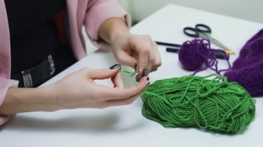 Çekici genç bir kadın beyaz bir stüdyoda yeşil çorap örüyor.