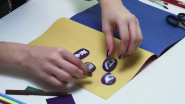 Kadın, masa üzerinde renkli kağıt ve yapıştırıcıdan bir el işi yapıyor.