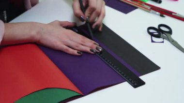 Kadının üst görünümü masadaki renk kağıdına çizgiler çizmek için kalem ve cetvel kullanır