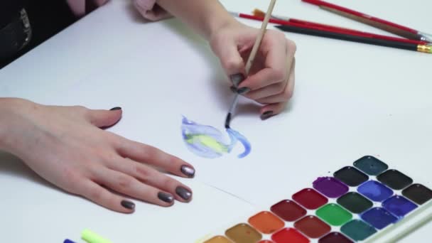 Närbild av kvinna ritar med akvareller på ett vitt papper vid bordet i en vit studio — Stockvideo