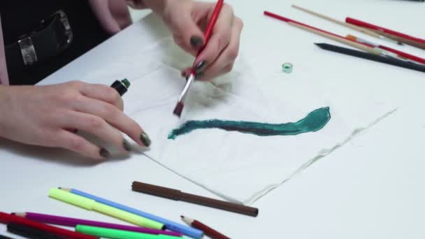 Vonzó fiatal nő rajzol egy zöld akril festékek egy fehér ruhát az asztalnál — Stock videók