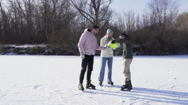 Jovens amigos bebem um chá quente depois de passeios de patinação no gelo no lago congelado na floresta — Vídeo de Stock