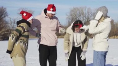 Noel Baba şapkalı dört arkadaş, ormanda büyük donmuş bir gölde buz pateni yaptıktan sonra kameraya poz veriyor.