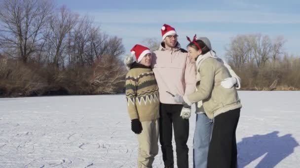 Quatro amigos no Natal Papai Noel fica juntos e tenta tirar uma selfie no telefone depois de passeios de patinação no gelo em um grande lago congelado na floresta — Vídeo de Stock