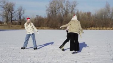 Noel Baba şapkalı genç mutlu arkadaşlar ormanda büyük donmuş bir gölde birlikte buz pateni yapıyorlar.