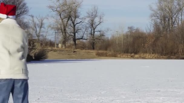 Young woman in christmas santa hat rides ice skating and talks on phone on frozen lake in forest — Stock Video