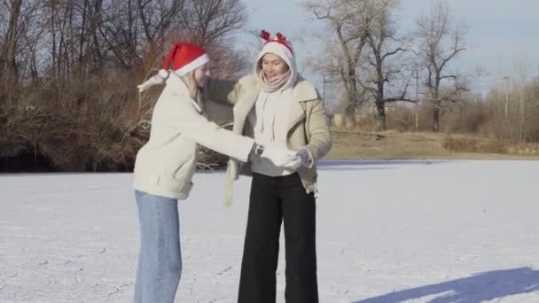 Dwie młode kobiety w świątecznych kapeluszach jeżdżą na łyżwach i łyżwach na lodzie — Wideo stockowe