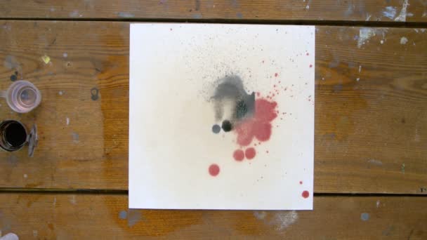 Góra widok trzech artystów są maluje abstrakcyjny obraz: jeden wlewa kilka kropli czarnego bólu na płótnie, drugi artysta używa sprayu wodnego, aby przenieść tę farbę, a trzeci wykorzystuje suszarkę — Wideo stockowe