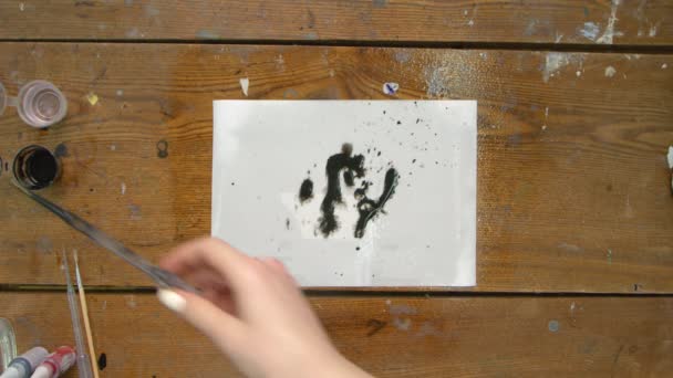 Vista superior de la artista pinta un cuadro abstracto, ella vierte unas gotas de dolor negro sobre lienzo húmedo y utiliza secador para moverlo y secarlo — Vídeo de stock