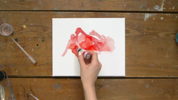 Vista superior de la artista pinta un cuadro abstracto, ella vierte unas gotas de dolor rojo a la lona húmeda y utiliza secador para moverla y secarla — Vídeo de stock