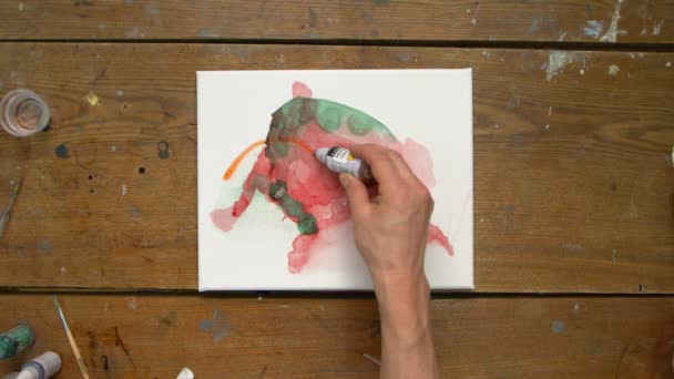 Ovanifrån av manliga konstnären målar en abstrakt bild, han använder pensel och en orange färg — Stockvideo