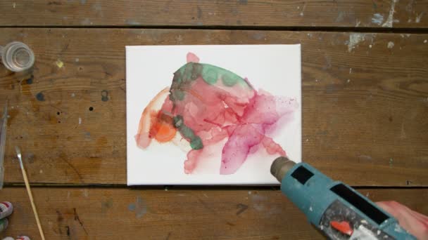 Vista superior da artista feminina pinta um quadro abstrato, ela usa secador para distribuir tintas e secá-lo — Vídeo de Stock
