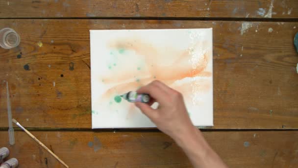Κορυφαία άποψη του αρσενικού καλλιτέχνη ζωγραφίζει μια αφηρημένη εικόνα, χρησιμοποιεί πράσινο χρώμα σε βρεγμένα καναρίνια και το διανέμει με πινέλο — Αρχείο Βίντεο