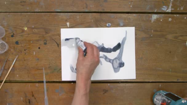 Κορυφαία άποψη του αρσενικού καλλιτέχνη ζωγραφίζει μια αφηρημένη εικόνα, χρησιμοποιεί μαύρη μπογιά σε βρεγμένα καναρίνια και τη διανέμει με πινέλο — Αρχείο Βίντεο