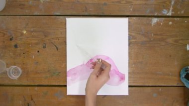 Sıvı Sanat. Soyut renkli tablolar. Kadın ressamın üst görüntüsü pipetten tuvale su döker ve boya fırçasıyla onu dağıtır.