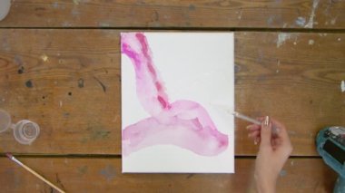 Sıvı Sanat. Soyut renkli tablolar. Kadın ressamın üst görüntüsü pipetten tuvale soyut bir resimle su döker ve onu dağıtmak için boya fırçası kullanır.