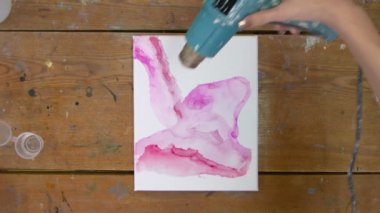 Sıvı Sanat. Soyut pembe resim. Kadın ressamın üst görüntüsü, pembe bir boyayı taşımak ve yeni pembe resmini kurutmak için kurutma makinesi kullanıyor.