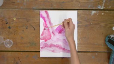 Sıvı Sanat. Soyut pembe resim. Kadın ressamın üst görünüşü, ıslak tuvale soyut pembe şekiller çizer.