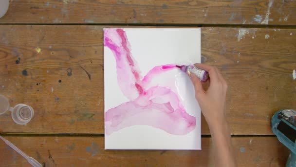 Ovanifrån av kvinnlig konstnär målar en abstrakt rosa bild, hon häller rosa färg från röret på våt duk — Stockvideo