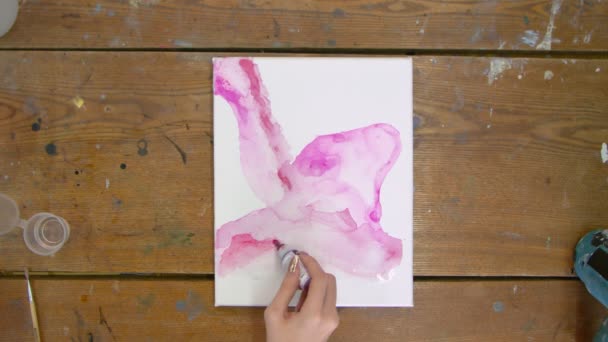 Kadın ressamın üst görüntüsü güzel, soyut bir tablo çizer, ıslak tuvale pembe bir tüp döker ve boya fırçasıyla onu dağıtır. — Stok video