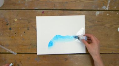 Erkek ressamın üstten görünüşü güzel, soyut bir tablo çiziyor, ıslak tuval üzerine mavi boya döküyor.