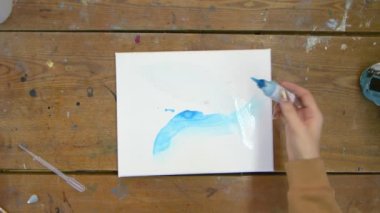 Kadın ressamın üst görüntüsü güzel soyut şekiller çizer, ıslak tuval üzerine mavi boya döker.