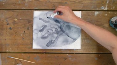 Sıvı Sanat. Soyut karanlık resim. Erkek ressamın üst görüntüsü pipetten tuvale su döker ve boya fırçasıyla onu dağıtır.