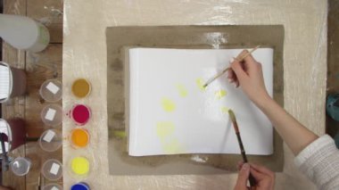 İki profesyonel ressamın üst görüntüsü Pastel kravat boyasını ıslak tuvale sarı boya ile boyamış. Sıvı Sanat.