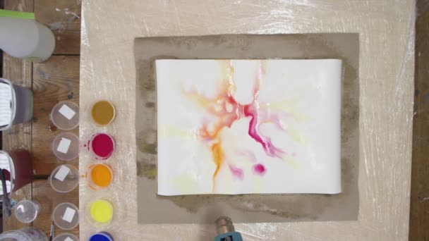 Top view of male artist paints Pastel tie dye picture with yellow and red paints on wet canvas. And He uses dryer to move liquid paints. Fluid Art. — Stock Video