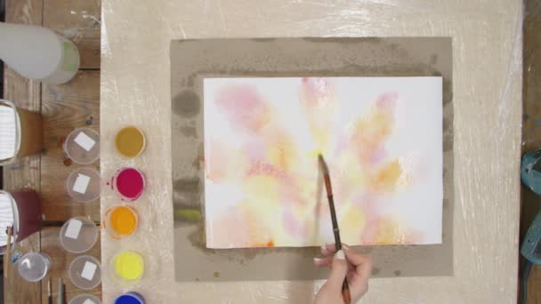 Vista superior de la artista femenina pinta cuadro de tinte de corbata Pastel con pinturas amarillas, rojas y naranjas sobre lienzo húmedo. Arte fluido. — Vídeos de Stock