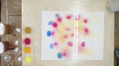 Erkek ressamın üst görüntüsü Pastel kravat boyası ya da Pastel kıvrımlı resimde ıslak tuval üzerinde mavi daireler çizer. Sıvı Sanat.