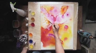 Sıvı Sanat. Soyut renkli tablolar. Erkek ressamın üst görünümü, ıslak tuvale soyut şekiller çizmek için boya fırçası kullanır.