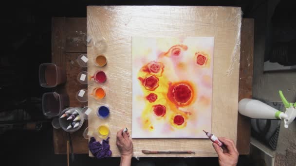 Vista superior de artista masculino pinta un cuadro abstracto, que vierte un montón de pocas gotas de pinturas rojas y negras a la lona húmeda — Vídeo de stock