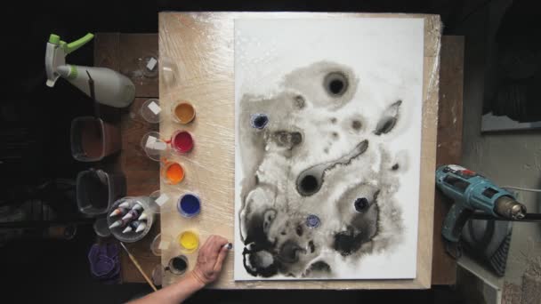 Вид зверху чоловічий художник малює абстрактну картину, він наливає кілька крапель чорно-синіх фарб на вологе полотно — стокове відео