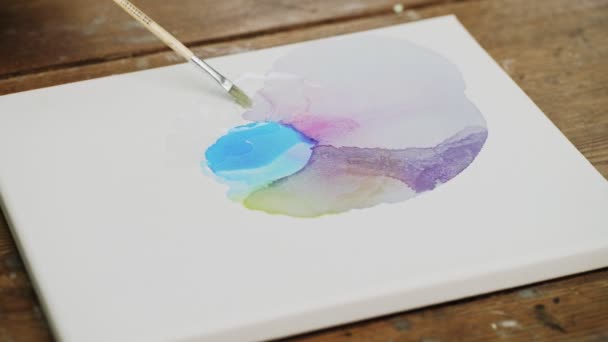 Fluide Kunst. Abstrakte farbenfrohe Malerei. Nahaufnahme einer Künstlerin, die Wasser auf die Leinwand gießt und mit dem Pinsel verteilt — Stockvideo
