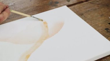 Erkek ressamın yakın çekimi soyut bir resim çizer, ıslak tentelere turuncu boya sürer ve boya fırçasıyla dağıtır.