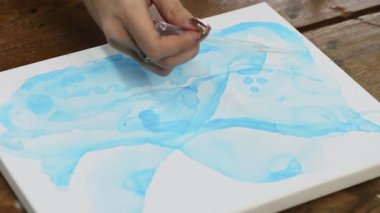 Sıvı Sanat. Soyut renkli tablolar. Kadın sanatçıya yakın çekim, pipetten tuvale mavi soyut resimli su döker
