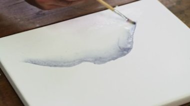 Erkek ressamın yakın çekimi soyut bir resim çizer, ıslak tuvale birkaç damla siyah boya döker ve boya fırçasıyla onu dağıtır.