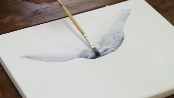 Közelkép férfi művész fest egy absztrakt képet, ő öntött néhány csepp fekete festék nedves vászon és használja ecsettel terjeszteni. — Stock videók