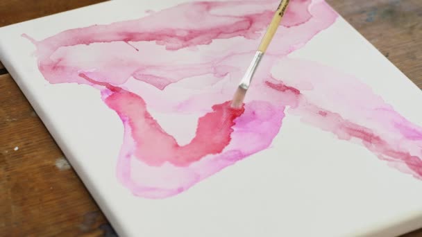 Close up of woman artist pinta um quadro abstrato, ela usa pincel para distribuir água em tela com tinta rosa — Vídeo de Stock