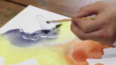 Sıvı Sanat. Soyut renkli tablolar. Erkek ressamın üstten görünüşü, siyah ve sarı renkli ıslak tuvale sarı boya döküyor.